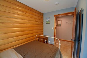 A bedroom with a wooden slat wall, a single bed with a metal frame, a small wooden nightstand, and a door with a natural wood finish. - Secluded Cabin w/ Dock Access in Pittsville (Pittsville)