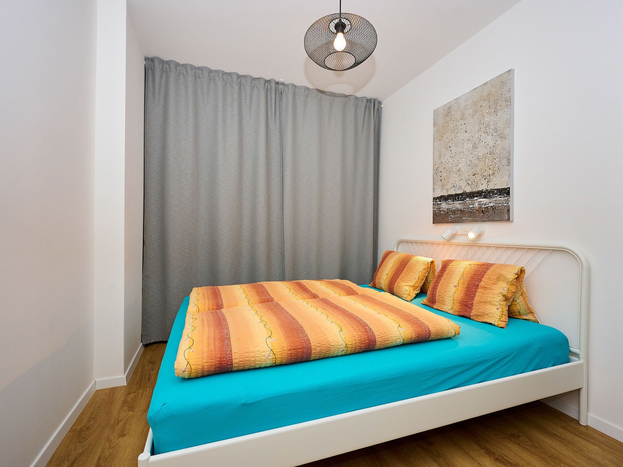 A bedroom with a bed, grey curtains, a wall art piece, and a hanging light fixture.