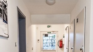 Ein Flur mit Fliesenboden, einer Tür mit Ausgangsschild, einem Feuerlöscher und einer wandmontierten Leuchte.