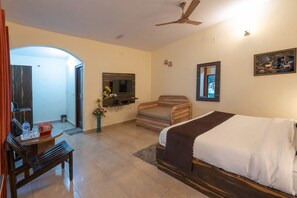 Quarto de hotel com cama, escrivaninha, cadeira, televisão na parede e ventoinha no teto.