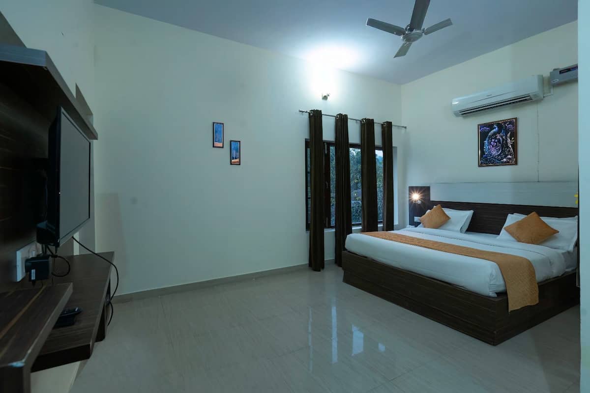 A hotel room with a bed, a TV, a ceiling fan, and an air conditioner.