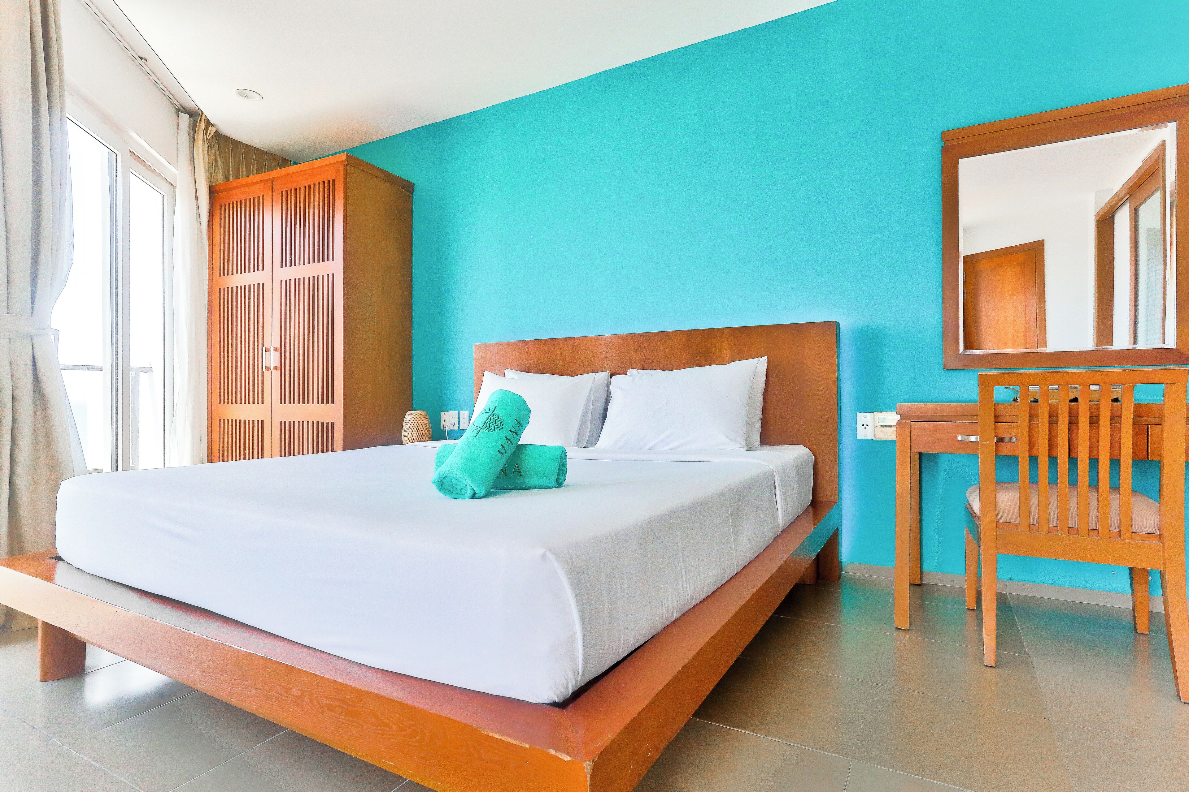 A hotel room with a bed, a wooden wardrobe, a desk, and a chair.