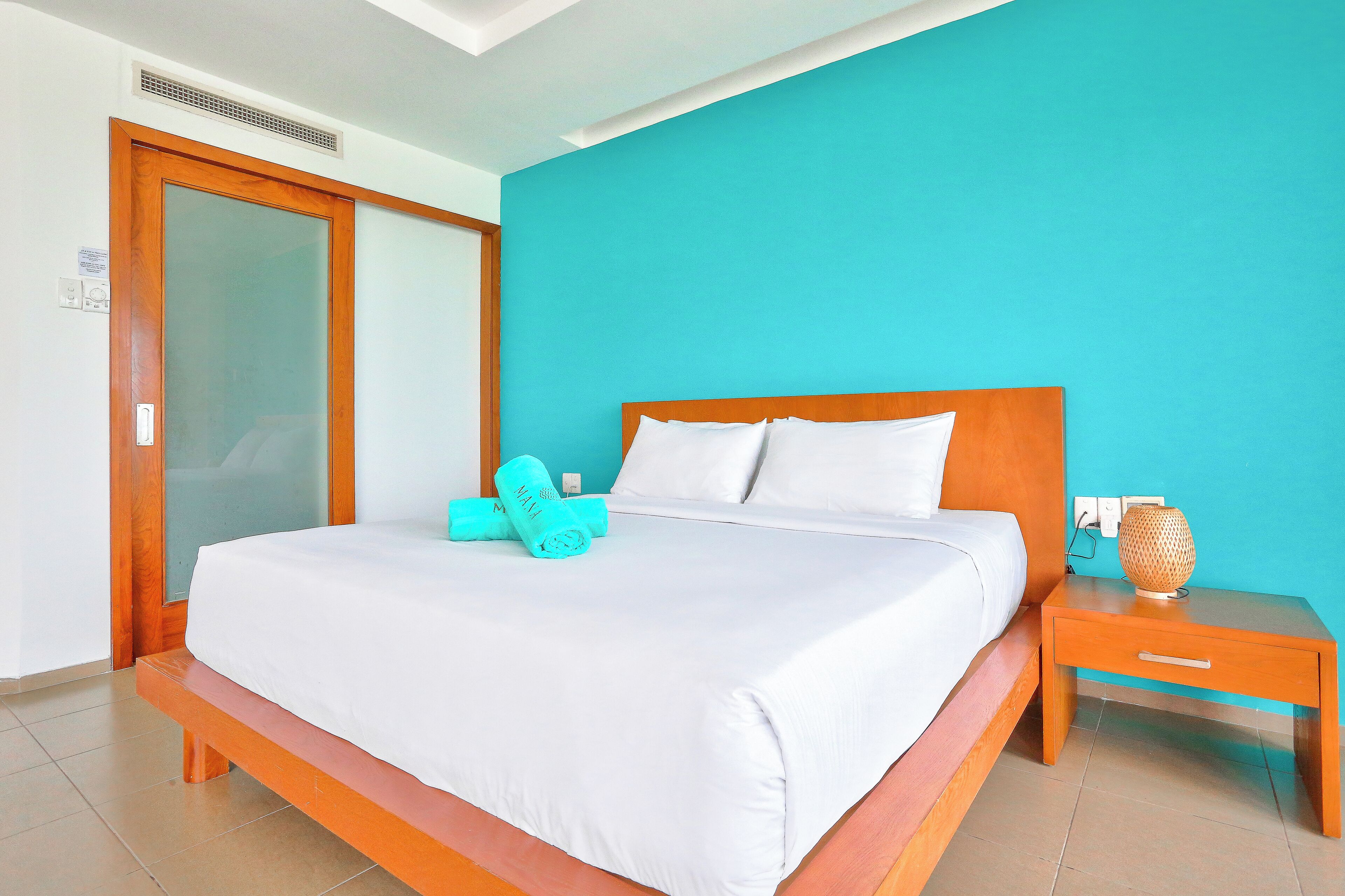 Un lit bien fait, avec du linge de lit blanc, une tête de lit en bois et un mur de couleur turquoise.
