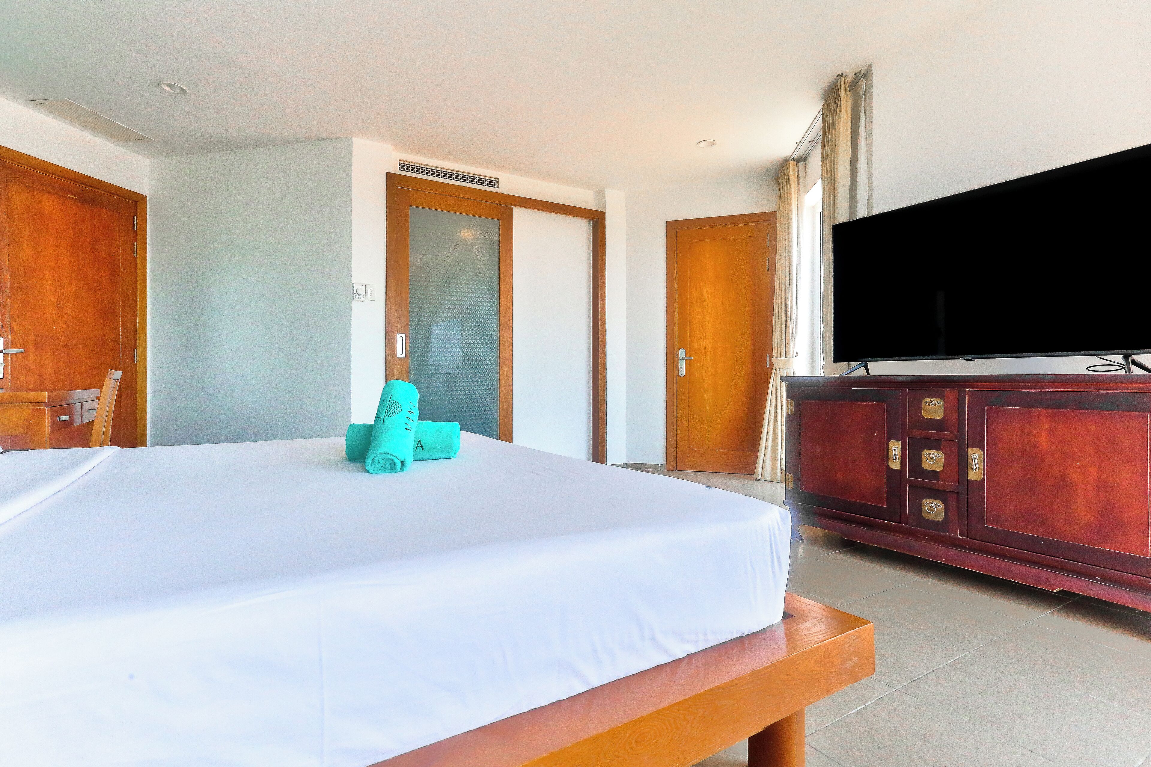 A hotel room with a bed, a television, a wooden cabinet, and a door.