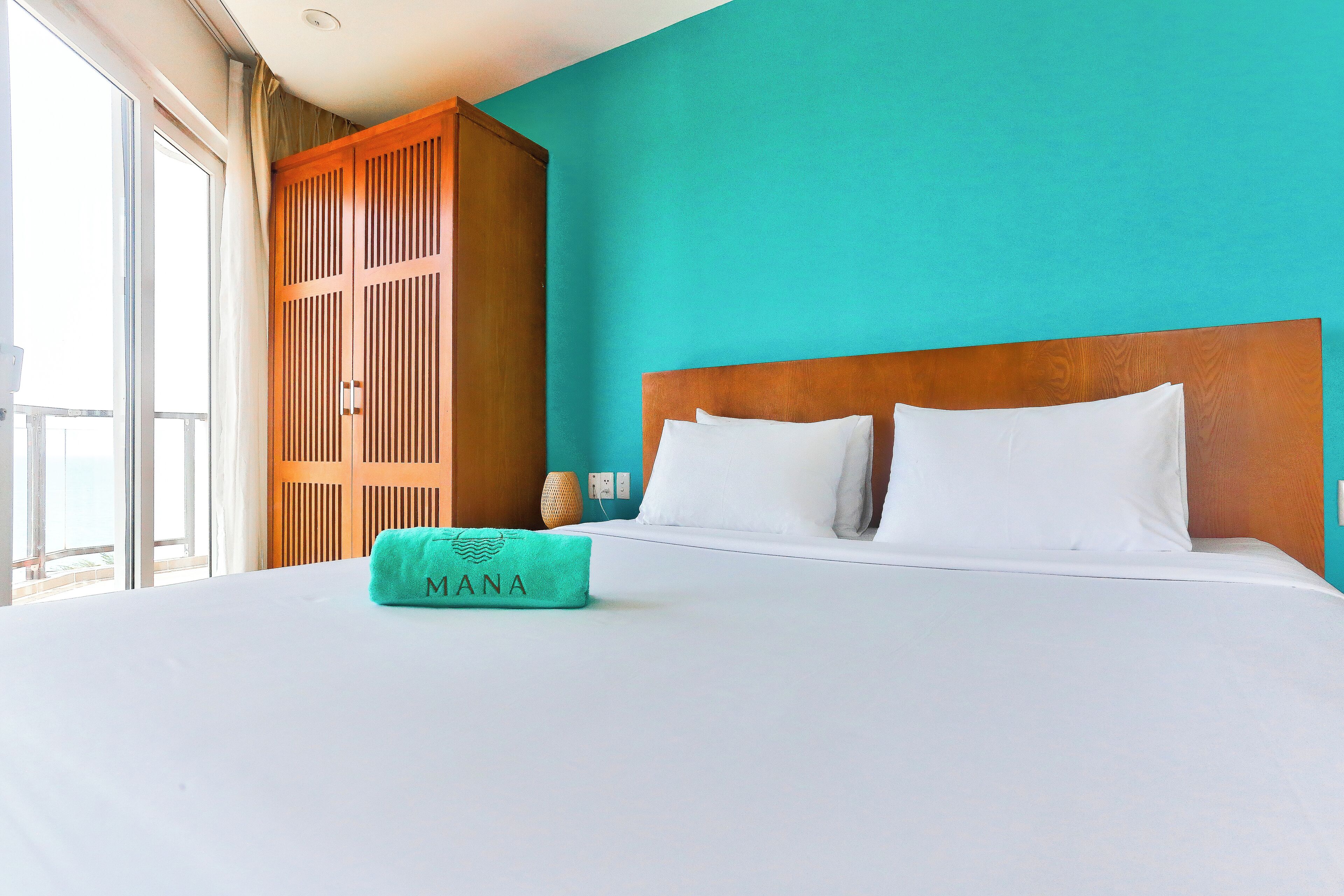 A hotel room with a large bed, teal walls, and a wooden wardrobe.