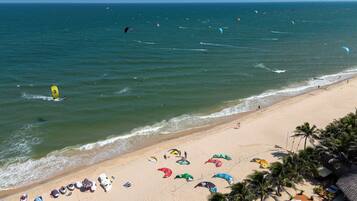 A beach with multiple kitesurfing activities and a sandy shore with umbrellas and beach chairs.