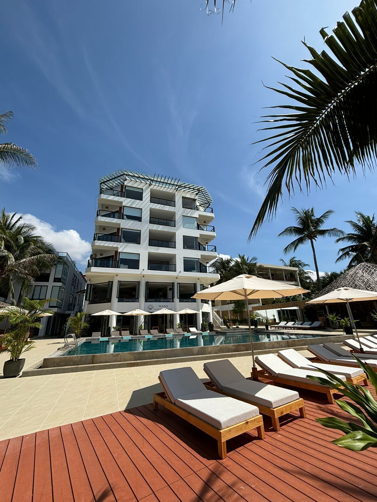Un hotel moderno con piscina, sillones de descanso y palmeras.