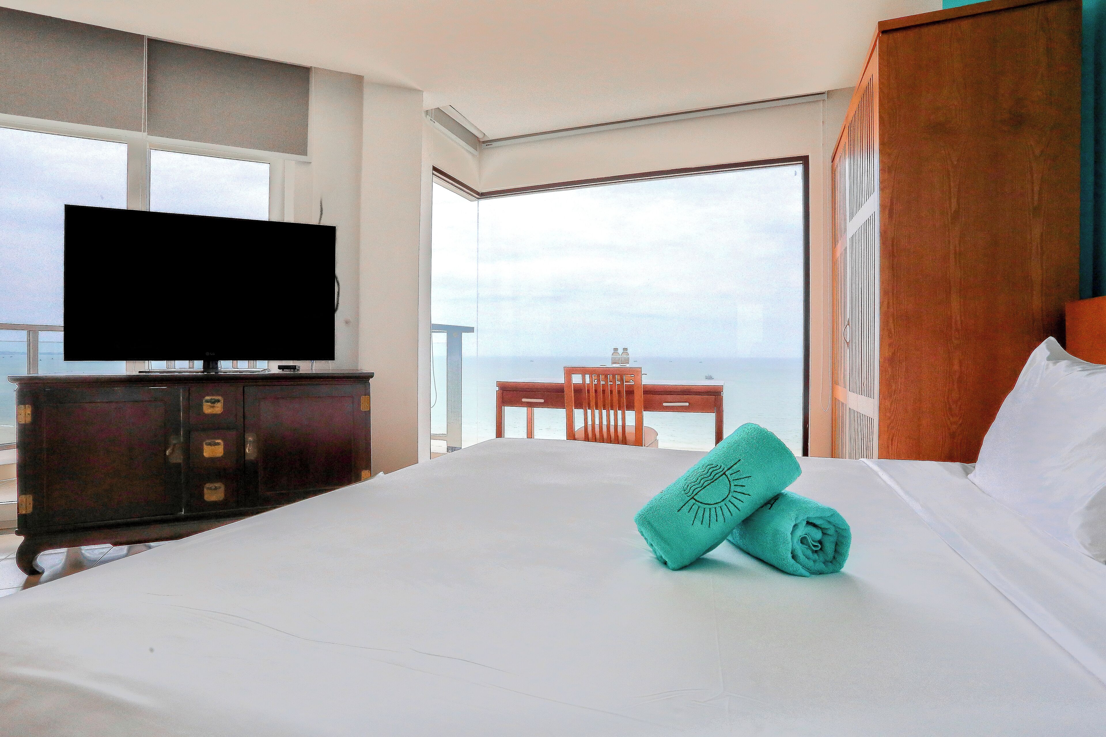 A hotel room with a large bed, a television on a wooden cabinet, a wooden chair, and a view of the ocean.
