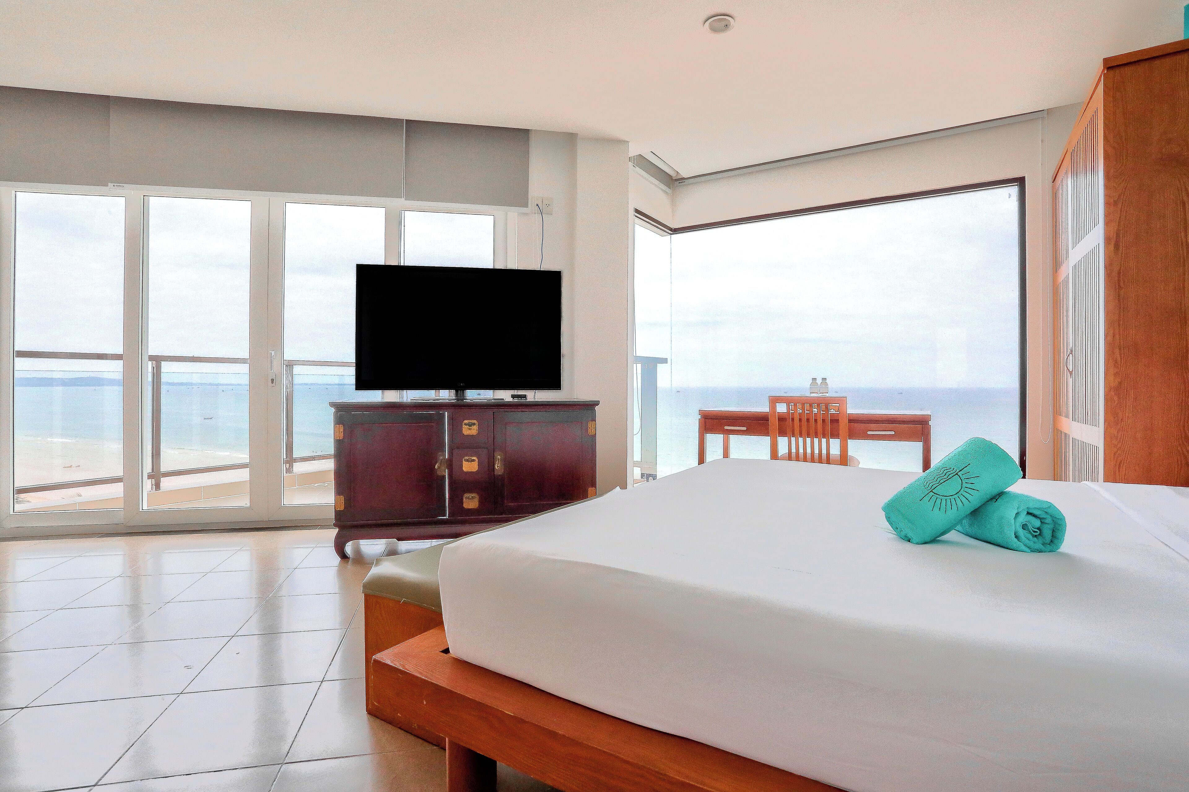 Una habitación de hotel con una cama grande, un televisor de pantalla plana, un escritorio de madera y vista al océano a través de amplias ventanas.