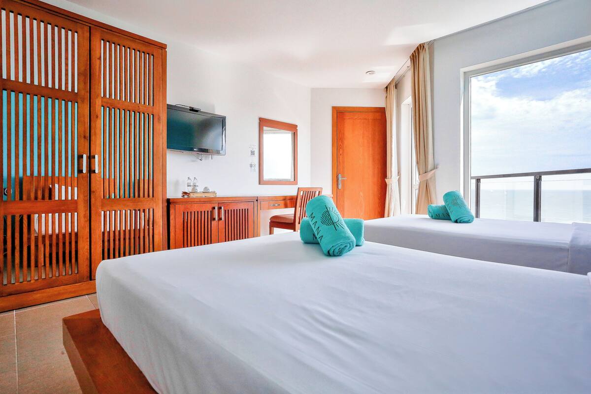 Ein Hotelzimmer mit zwei Betten, einem Fernseher, einem Schreibtisch und einem Fenster mit Blick.