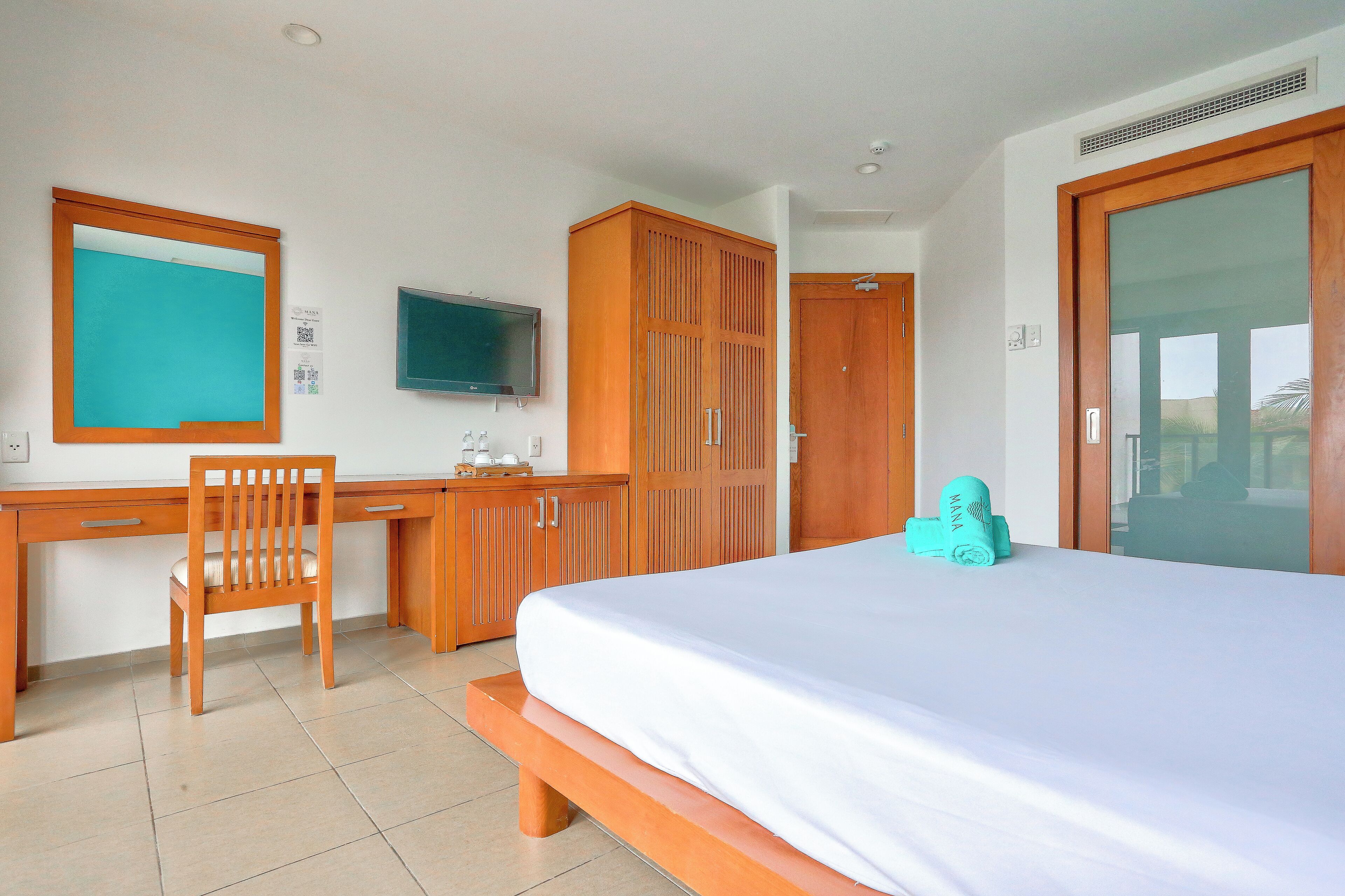 Ein Hotelzimmer mit Bett, Schreibtisch aus Holz, Stuhl, Fernseher, Kleiderschrank und einem Fenster mit Aussicht.