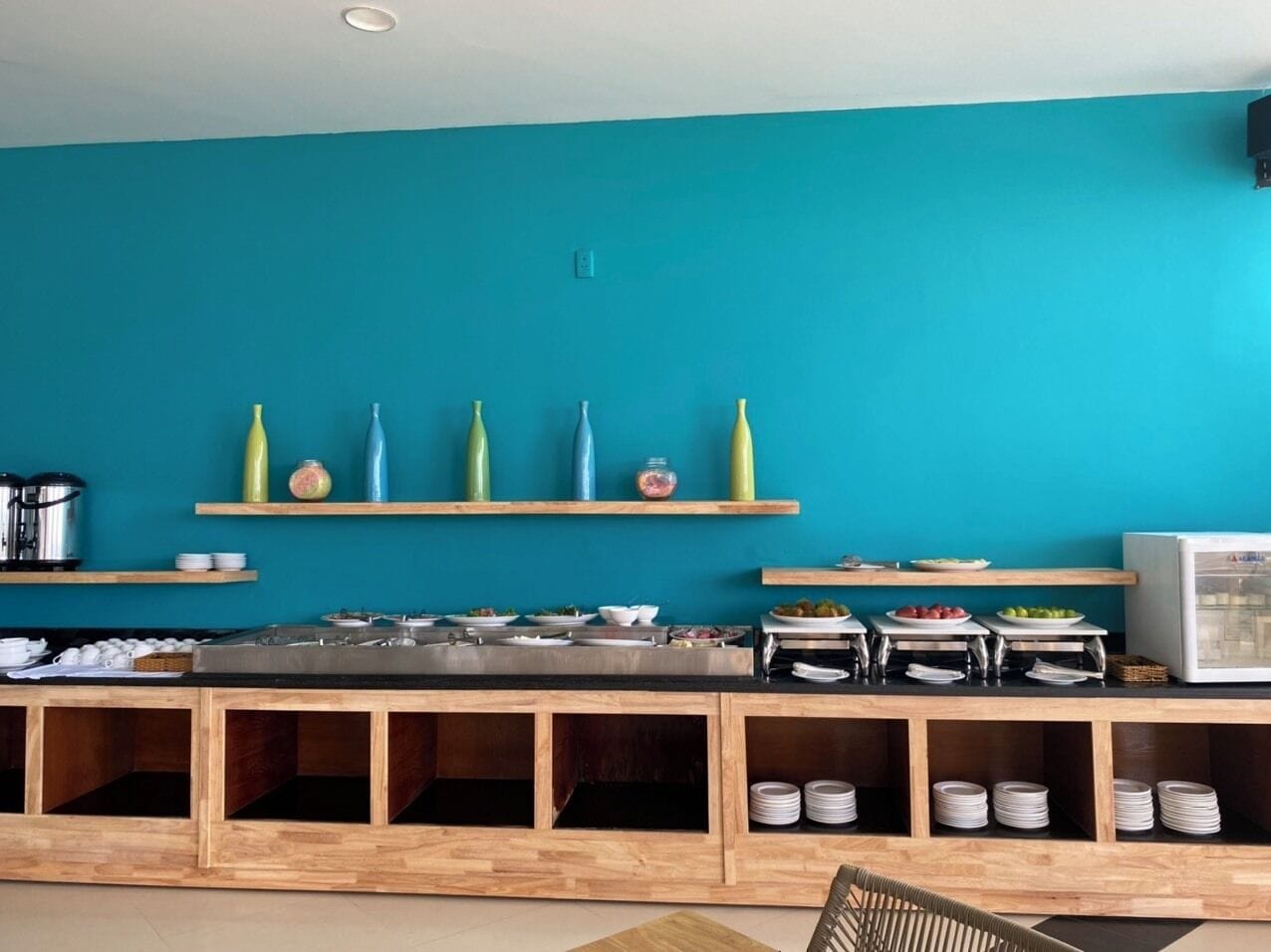 A kitchen area with teal walls, wooden shelves, and various kitchen appliances and utensils.