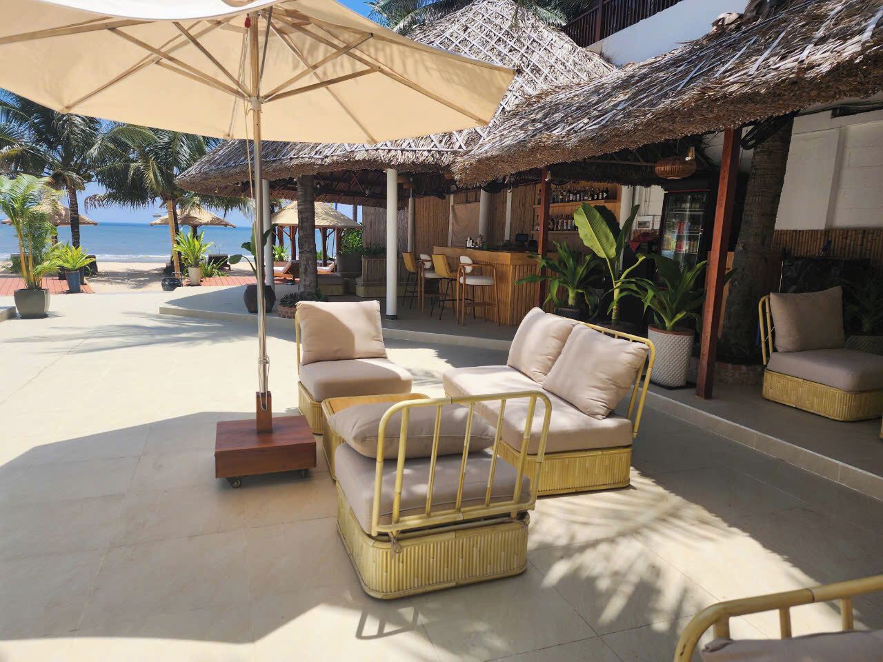 A beachside lounge with wicker furniture, a bar, and thatched umbrellas.