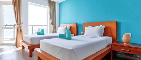 A hotel room with two beds, a wooden nightstand, a bedside table, and a window with curtains.