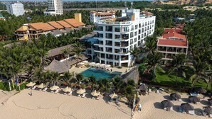 A multi-story hotel with a pool, surrounded by palm trees and beach umbrellas. - Mana Mui Ne Beach Resort & Spa (Mui Ne)
