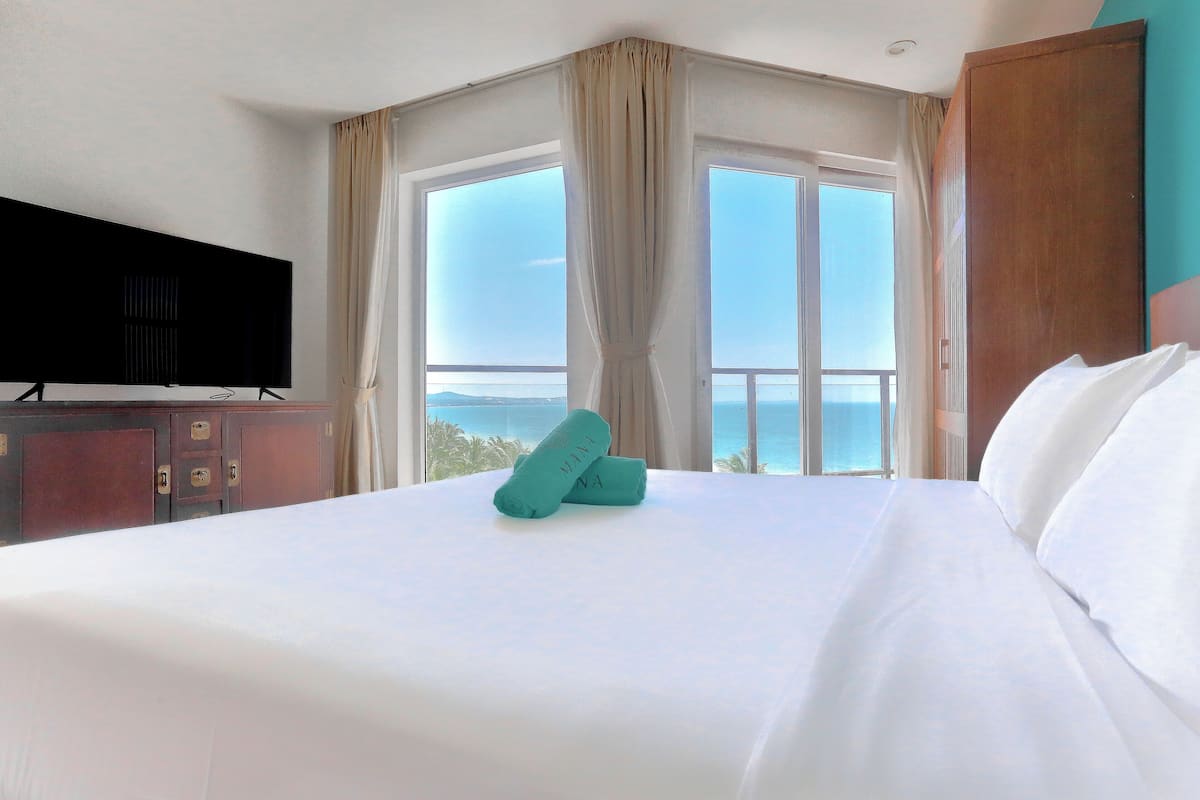 Ein Hotelzimmer mit einem großen Bett, einem Fernseher links und Meerblick durch die Fenster.