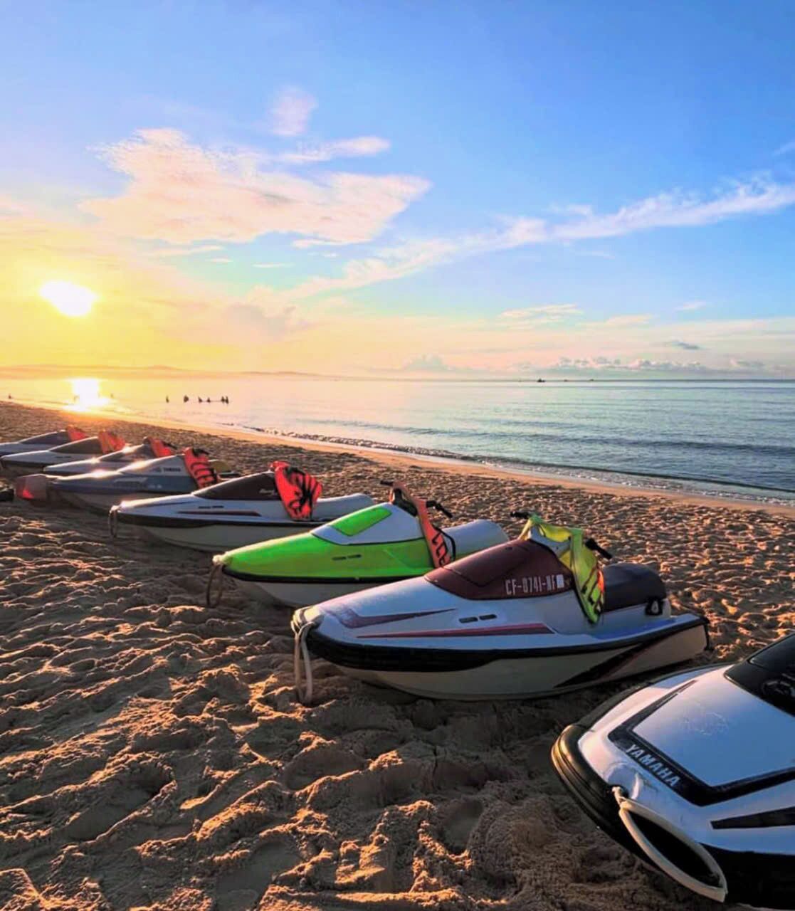 Waterscooters op een zandstrand, met een zonsondergang op de achtergrond.