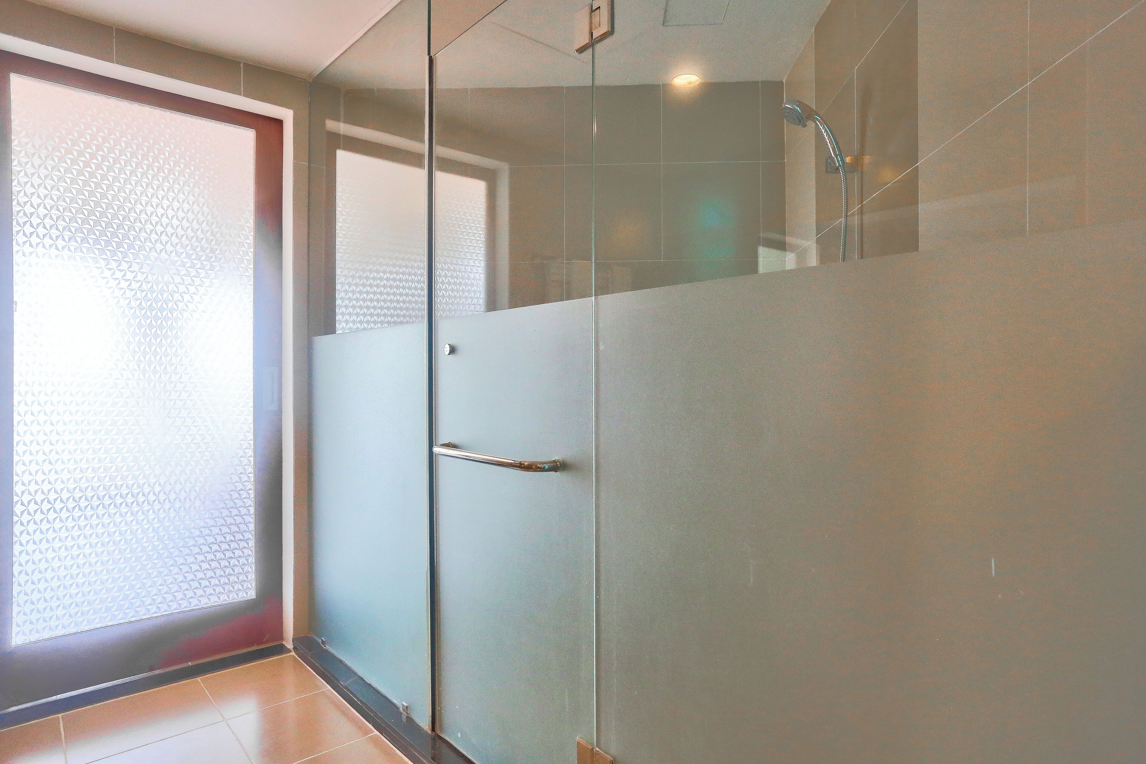 Un baño moderno con cabina de ducha de vidrio, un cabezal de ducha visible y una puerta con pomo.