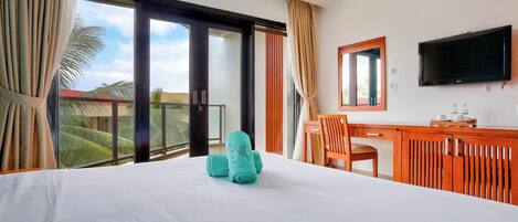 A hotel room with a bed, a desk, a chair, a TV, and a balcony with a view of palm trees.