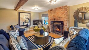 A living room with a brick fireplace, a sofa set, a round coffee table, and a large abstract painting. - Great Easton Lodge (Great Easton)