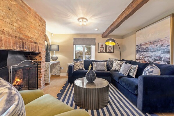A cozy living room with a fireplace, a blue sofa set, a round coffee table, and a striped rug.
