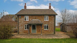A two-story stone house with a central entrance, a small porch, and a chimney. - Great Easton Lodge (Great Easton)