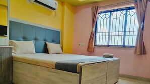 A bedroom with a bed, a window with curtains, an air conditioning unit, and a wall socket. - Hotel Mahal & Restaurant (Kalyani)
