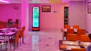 A restaurant with pink lighting, a Coca-Cola refrigerator, and orange chairs. - Hotel Mahal & Restaurant (Kalyani)