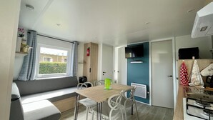 Cocina compacta con comedor, ventana con cortinas, televisor integrado y estufa.