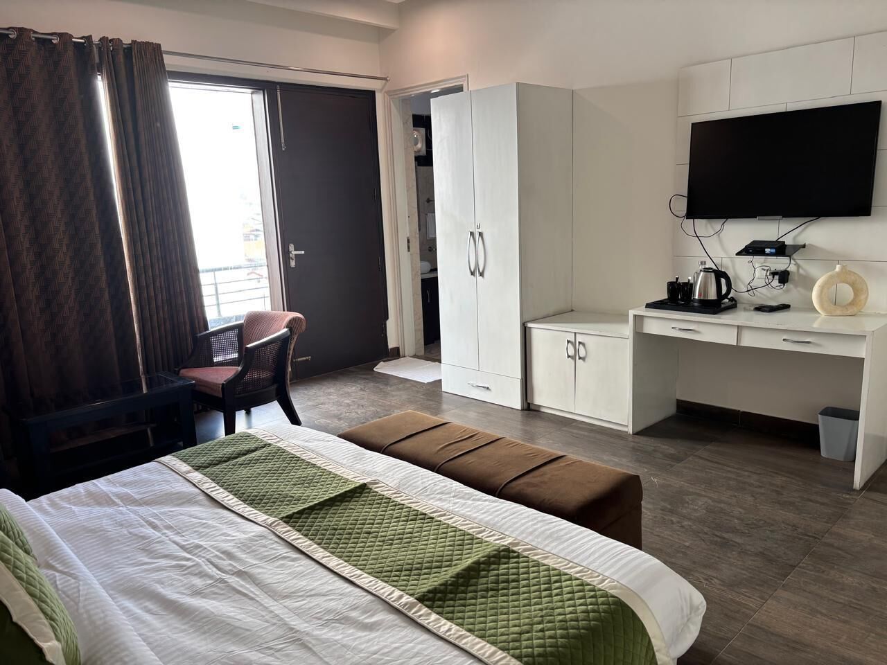 A hotel room with a bed, a desk, a chair, a television, and a wardrobe.