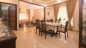 Un comedor con una mesa dispuesta para cuatro personas, rodeada de sillas. Hay un ventilador de techo, un aparador de vidrio con objetos decorativos y una puerta que da a otra habitación.