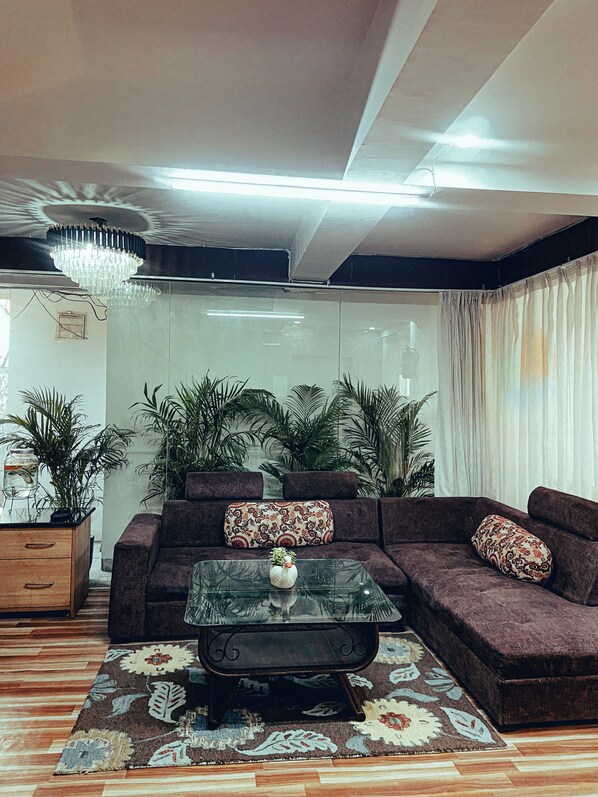 A living room with a sectional sofa, a glass coffee table, and a chandelier. - TIM Stayz Deharadun (Dehradun)