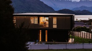 Una casa moderna con fachada de madera, ventanas amplias y vistas a montañas nevadas.