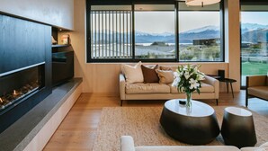 Una sala de estar moderna con chimenea, un sofá, una mesa de centro y vistas a montañas a través de amplios ventanales.