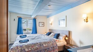 Un dormitorio con cama, mesitas de noche, un ventanal con cortinas y lámparas fijadas a la pared.