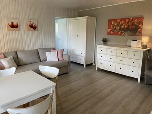 A modern living room with a sofa, a dining table, a white cabinet, and a painting on the wall. - Holiday Home 'am Rosenhag' with Private Terrace, Private Garden and Wi-Fi (Berlin)