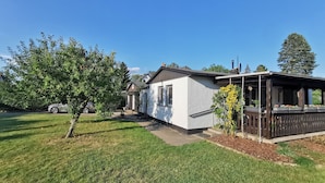A residential property with a white exterior, a covered outdoor area, and a well-maintained lawn.
