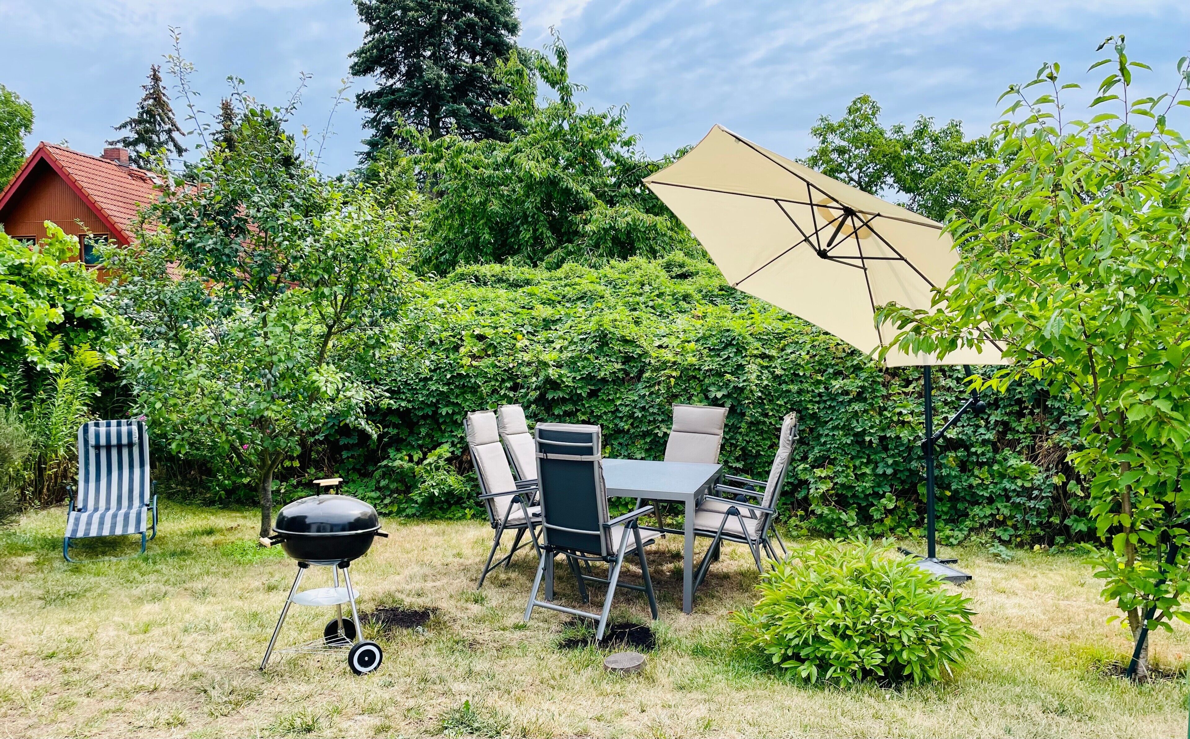 Un cortile con un barbecue, un tavolo con sedie e un grande ombrellone.
