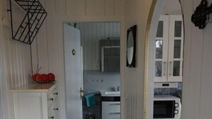 A narrow hallway leading to a kitchen with white cabinets, a microwave, and a blue mat on the floor.