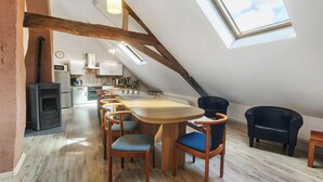 Un comedor con una larga mesa de madera y sillas, un sillón de cuero negro, una mesita y un tragaluz.