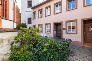 Un bâtiment doté d’une terrasse carrelée, d’une table avec des chaises et d’une porte avec un portail en métal.