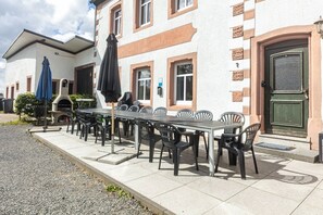 Ein Essbereich im Freien mit einem langen Tisch und Stühlen, einem Grill und Sonnenschirmen.