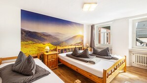 Een slaapkamer met twee bedden, een groot raam en een sfeervol muurschildering.