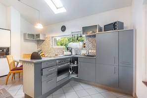 A modern kitchen with grey cabinets, a built-in oven, a microwave, and a window with a view of greenery. - Large Holiday Home 'Engelsdorf' with Private Terrace and Wi-Fi (Zweifelscheid)