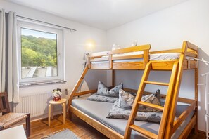 En våningssäng med utsikt över en skog genom ett fönster, ett litet bord och en stol.