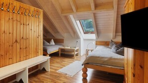 Une chambre située dans un espace de type « loft », avec un plafond en pente, des poutres en bois, une lucarne, un lit, un banc, une télévision et une table de chevet.