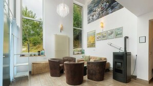 Un salon doté d’une cheminée, de grandes fenêtres et offrant une vue sur la verdure environnante.