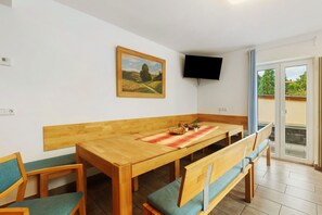 Un coin repas avec une table en bois, des bancs, un tableau accroché au mur et un téléviseur fixé au-dessus.
