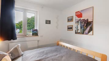 Et soveværelse med en seng, et vindue med gardiner, en radiator og billeder på væggen.