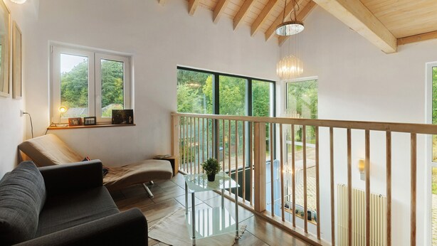 Un intérieur moderne avec un canapé, une table en verre et un balcon doté d’une balustrade en bois.